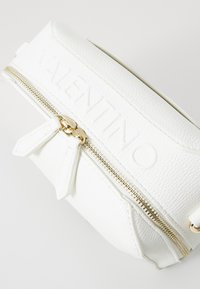 Vit läderhandväska med präglad "VALENTINO"-logotyp, guldbeläggning på dragkedjan, dubbla dragkedjeförare och texturerad yta.