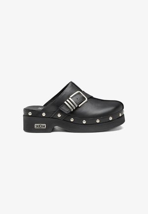 Zoccolo slip-on in pelle nera con fibbia argentata, borchie metalliche lungo la suola e logo metallico del marchio sul tallone.
