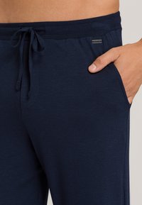 Navy blauwe joggerbroeken van zacht materiaal, met een elastische tailleband met een trekkoord en zijzakken. Minimale logosticker zichtbaar.