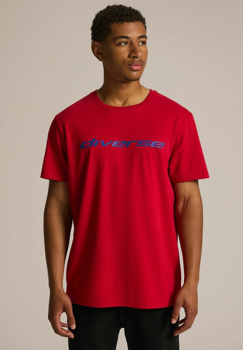 Czerwona bawełniana koszulka z krótkim rękawem i okrągłym dekoltem. Na przodzie widoczny niebieski napis "diverse", gładka tekstura oraz regularny krój.