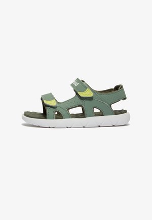Green synthetic sandal with multiple cutouts, Velcro straps, and white rubber sole featuring a textured footbed. Accents of yellow detail.
