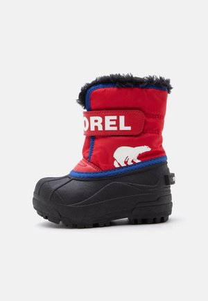Botte d'hiver rouge et noire avec doublure en fourrure noire, bordure bleue, logo ours polaire blanc et sangle blanche "SOREL" sur le dessus.