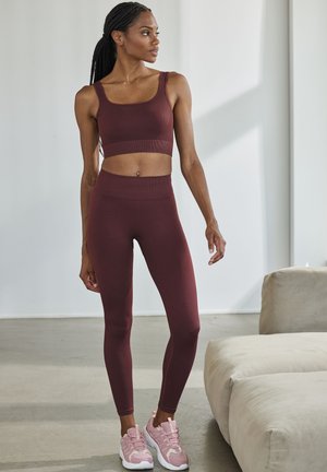 Burgundy ribbed sports bra paired with matching high-waisted leggings. Worn with pink lace-up athletic shoes, showcasing a smooth texture.