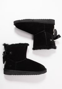 Botines de ante negro con ribete de pelo, acento de cinta y suela de goma texturizada. Exterior suave con forro interior de felpa.