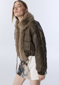 Bruine leren bomberjack met een bontkraag, voorzien van een gestikte ontwerp, drukknoopsluiting en twee voorzakken. Draagt over een graphic rok.