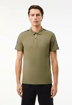 Polo de color verde oliva, de manga corta, con cuello, con acentos de patrón en blanco y negro en los hombros y un pequeño logotipo bordado en verde.