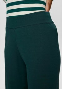 Pantalons larges en vert foncé avec une taille côtelée, présentant une texture lisse et sans motifs ni accessoires visibles.