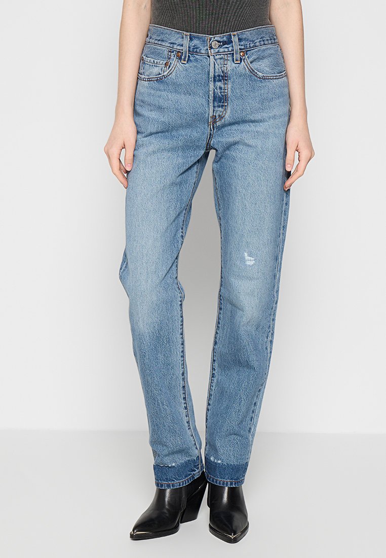 Jeans in denim blu chiaro con vestibilità a gamba dritta, vita alta, leggere abrasioni e passanti per cintura, abbinati a stivaletti neri con punta affusolata.