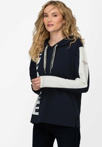 Marineblå hættetrøje med kontrasterende hvide ærmer, prydet med logoprint og snore. Blødt stof, afslappet pasform og sideskår i kanten.