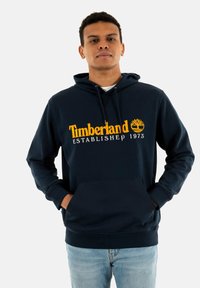 Sudadera azul marino con bolsillo tipo canguro, capucha con cordón y gran logo amarillo de Timberland con emblema de árbol, fabricada con tejido suave.