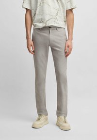 Ljust grå, texturerade byxor med rak bendesign. Har en framknappstängning och sidofickor. Kombineras med beige sneakers.