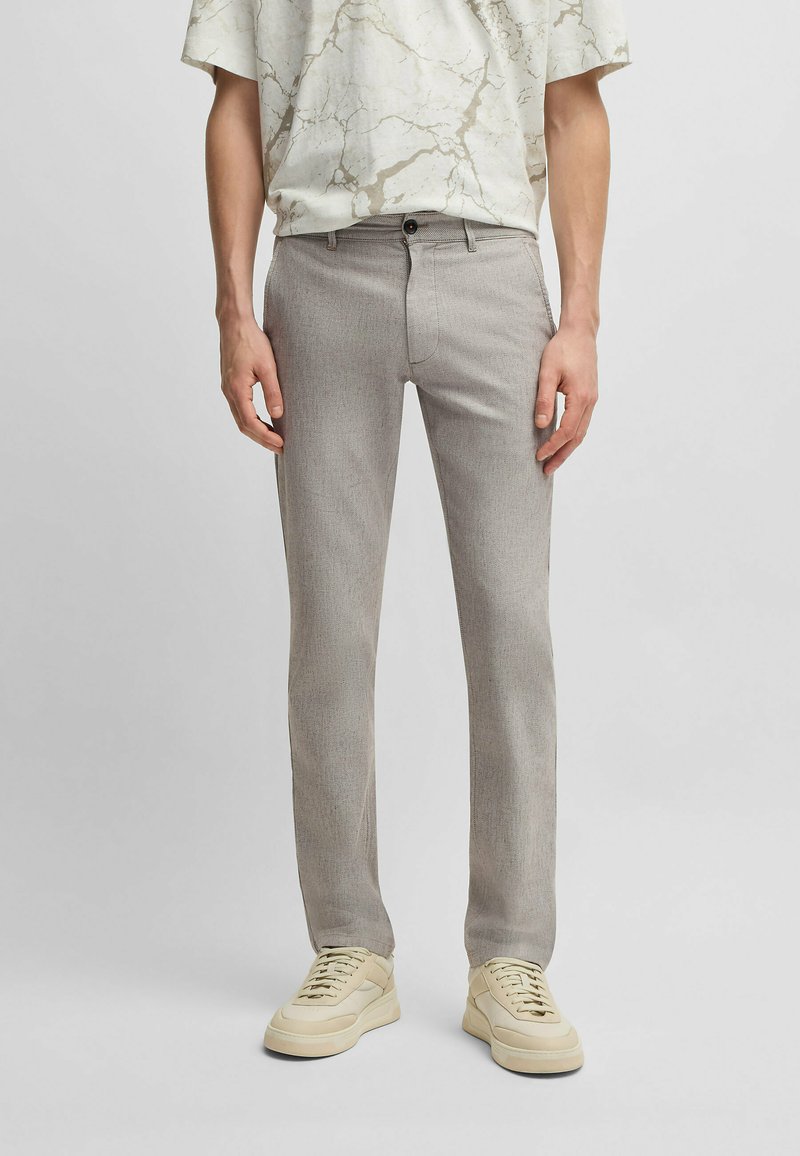 Ljust grå, texturerade byxor med rak bendesign. Har en framknappstängning och sidofickor. Kombineras med beige sneakers.