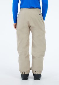 Beige sneeuwbroek met elastische tailleband, verstelbare boorden en verstevigde zoom. Soepele textuur en comfortabele pasvorm, geschikt voor winterse omstandigheden.