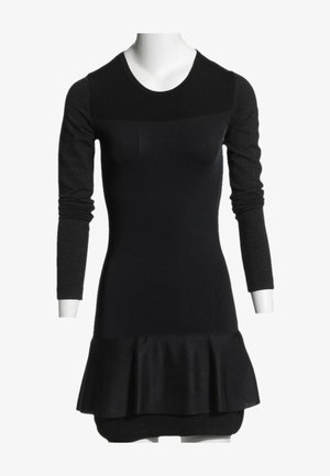 Robe noire ajustée à manches longues avec un col rond et un bas évasé à volants, présentée sur un buste de mannequin blanc.