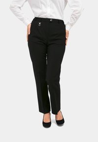 Zwarte op maat gemaakte broeken met een slim fit, met een zilveren accent op de tailleband en voorplooien, gecombineerd met zwarte gesloten schoenen.