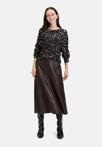 Dzianinowy sweter w czarno-tanowy wzór o oversize'owym kroju w zestawieniu z długą, ciemnobrązową skórzaną spódnicą oraz wysokimi, błyszczącymi czarnymi botkami.