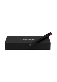 Crni Hugo Boss olovka na crnoj prezentacijskoj kutiji. Olovka ima teksturirani držač i crveni naglasak na kopči.