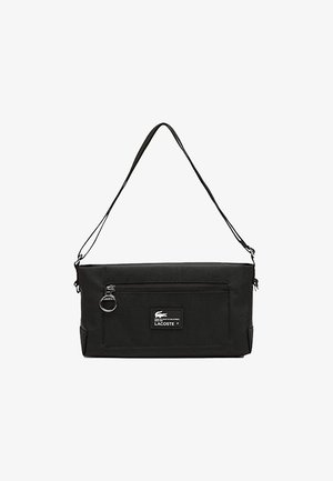 Sac bandoulière en tissu noir avec une fermeture éclair sur le dessus, une bandoulière amovible, une poche zippée à l'avant et un écusson du logo Lacoste à l'avant.