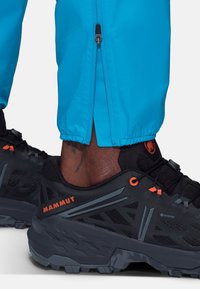 Svart vandringsko med strukturerad mesh, grå accenter och orange logotyp. Blå byxor med elastiska muddar och sidodetalj med dragkedja.