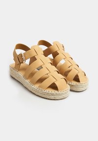 Sandali in pelle color cuoio con design a fascia incrociata, fibbia regolabile alla caviglia e suola avvolta in juta. Presentano una finitura testurizzata e la punta aperta.