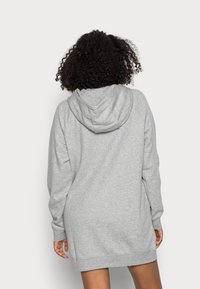 Grå sweatshirtklänning med huva, långa ärmar och lös passform. Mjuk tygtextur, når till mitten av låret, inga synliga mönster.