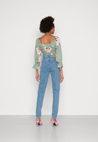 Blusa floral verde-claro com mangas bufantes e costas abertas, combinada com jeans de cintura alta azul-claro e sapatos de salto aberto rosa.