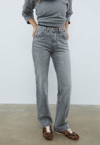 Sive jeans z ravnimi hlačnicami, z lahkotnim zbledelostjo in subtilnim whiskeringom. Kombinirani z supergami v leopardjem vzorcu.