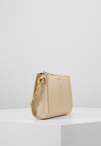 Mała, złota torebka skórzana z fakturowanym wykończeniem. Posiada złoty łańcuszek jako pasek oraz zamek błyskawiczny, prostokątny kształt z zaokrąglonymi brzegami.