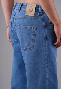Hellblaue Jeans aus Denim mit hoher Taille, ausgestattet mit hinteren Taschen, einem Lederlabel und hardwaredetails in Kupferfarbe.
