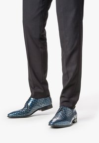 Scarpe con una texture blu a motivo squamato. Finitura lucida e tacco basso, abbinato a pantaloni neri su misura.