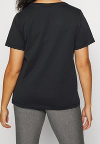 Czarny bawełniany t-shirt z krótkimi rękawami, okrągłym dekoltem i prostym brzegiem. Noszony z szarymi legginsami, prezentujący luźny krój i gładką teksturę.