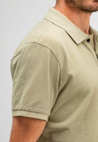 Khakifarbendes Polohemd aus strukturiertem Stoff, mit kurzen Ärmeln und klassischem Kragen mit zwei Knöpfen. Schlichtes und figurbetontes Design.