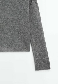 Manche et partie supérieure du torse d’un pull en maille gris à manches longues, montrant un tissu doux et texturé sur fond blanc.