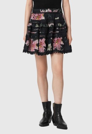 Mini-jupe courte noire à volants avec imprimé floral rose et bordure en dentelle, portée avec des bottines noires à fermeture éclair latérale.