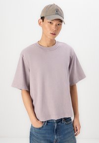 Lilac gray oversized cotton t-shirt with short sleeves, round neckline, and visible stitching, paired with a light brown baseball cap.