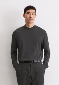 Długi rękaw, ciemnoszara bawełniana koszula z wysokim kołnierzem i prążkowanymi mankietami, zestawiona z pasiastymi, ciemnoszarymi sztruksowymi spodniami i czarnym paskiem.