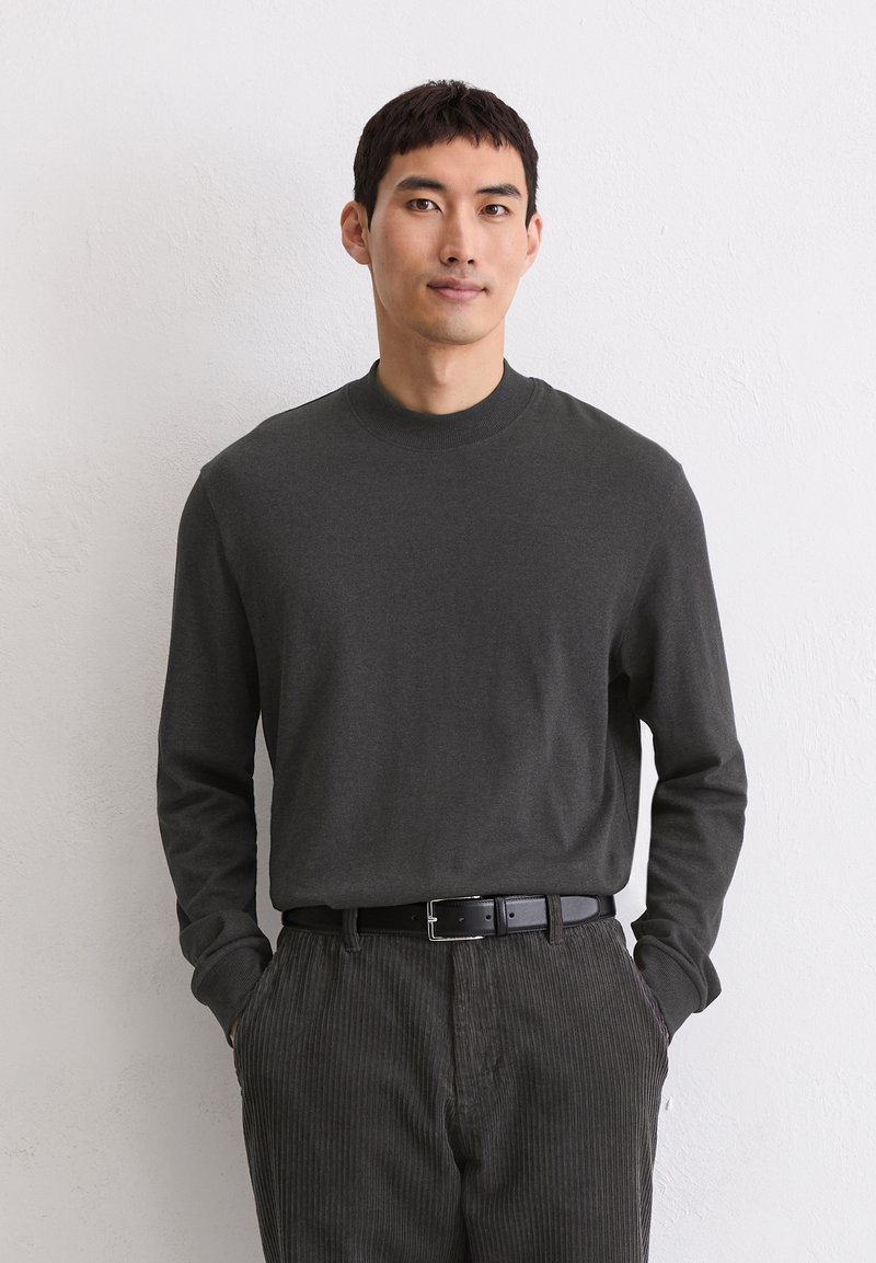 Długi rękaw, ciemnoszara bawełniana koszula z wysokim kołnierzem i prążkowanymi mankietami, zestawiona z pasiastymi, ciemnoszarymi sztruksowymi spodniami i czarnym paskiem.