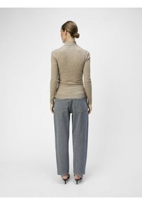 Beżowy dopasowany sweter z golfem w połączeniu z luźnymi niebieskimi dżinsami. Stylizacja zawiera eleganckie, czarne szpilki. Prosty design, minimalne detale.