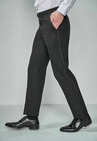 Pantalons noirs ajustés avec une coupe slim, en tissu texturé. Présentent des poches latérales et un design à jambes droites, associés à des chaussures de ville noires.