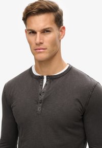 Dunkelgraues Langarm-Henley-Shirt mit Rundhalsausschnitt, fünfknöpfiger Knopfleiste und kontrastierendem weißen Innenkragen und -manschetten. Weicher Stoff.