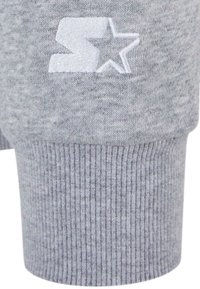 Tejido de sudadera gris con puños acanalados. Presenta una estrella bordada en blanco y la letra "S" en el puño. Textura suave con un patrón jaspeado.