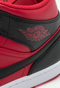 Close-up van een rode en zwarte Air Jordan sneaker die de leertextuur, het gevleugelde basketballogo, de stiksels en de witte zoolrand toont.