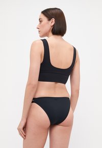 Black bikini set featuring a fitted top with wide straps and high-waisted bottoms, made from smooth fabric with minimalist design and no patterns.