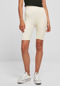 Beige katoenen fietsbroek met hoge taille, een gladde textuur en een knie-lange pasvorm, gecombineerd met casual witte canvas sneakers.