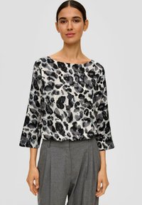 Blouse légère et fluide avec un imprimé léopard noir et gris sur un fond crème. Dotée d'un décolleté large et de manches trois-quarts.