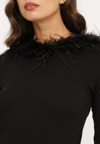 Zwart langarmtop met een weelderige zwarte verenrand rond de halslijn, met een getailleerd ontwerp en een gladde textuur.