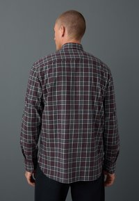 Long-sleeved, dark plaid shirt featuring burgundy base with white and navy intersecting lines, rounded hem, and buttoned cuffs.