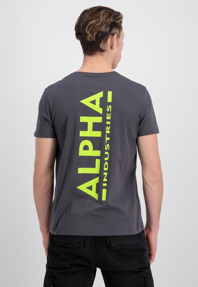 Grå bomulds t-shirt med et stort vertikalt neongrønt "ALPHA" print på ryggen, korte ærmer og en klassisk rund halsudskæring.