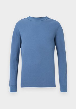 Plava rebrasta majica dugih rukava s okruglim izrezom i uskim manžetama. Glatka tekstura s dosljednim uzorkom kroz cijelu površinu.