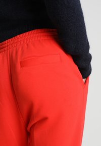 Punaiset verkkarit pehmeästä kankaasta, jossa on joustava vyötärö ja pieni sivutasku oikeassa takapuolessa.